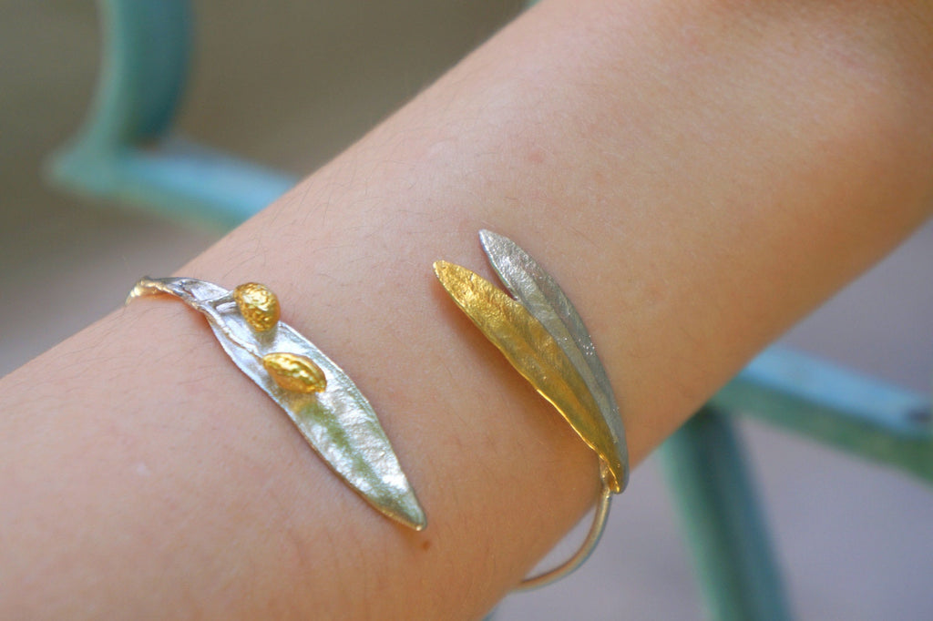 A bracelet with two leaf-shaped charms made of metal, one gold and one silver, is worn on a person's wrist.