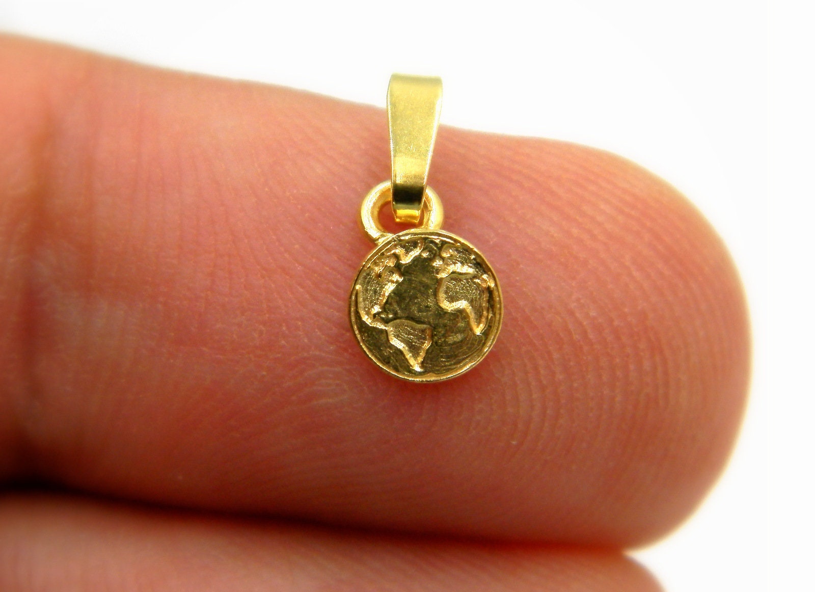 A small gold-colored charm or pendant is being held in a person's fingers, with a detailed image of a world map on it.