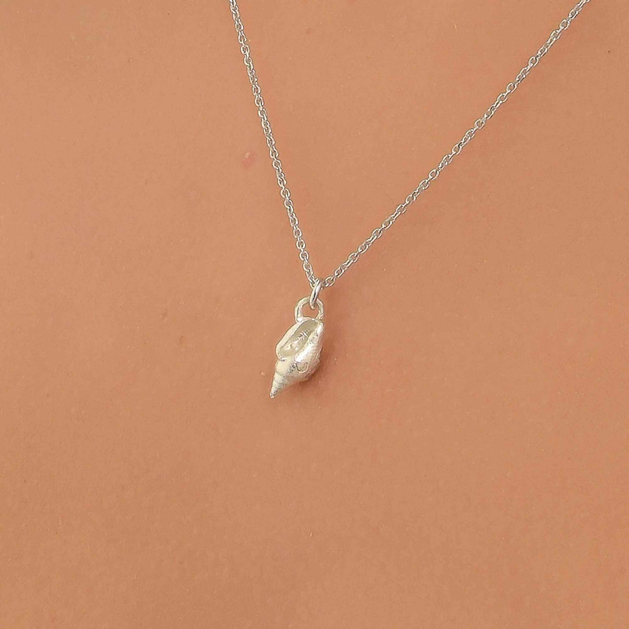 A silver necklace with a small pendant is shown against a peach-colored background.