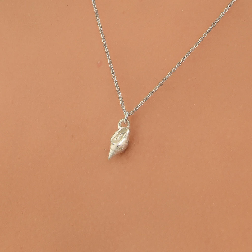 A silver necklace with a small pendant is shown against a peach-colored background.