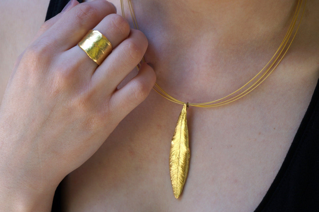 A close-up of a person's hand wearing a gold ring and necklace with a large gold leaf pendant.