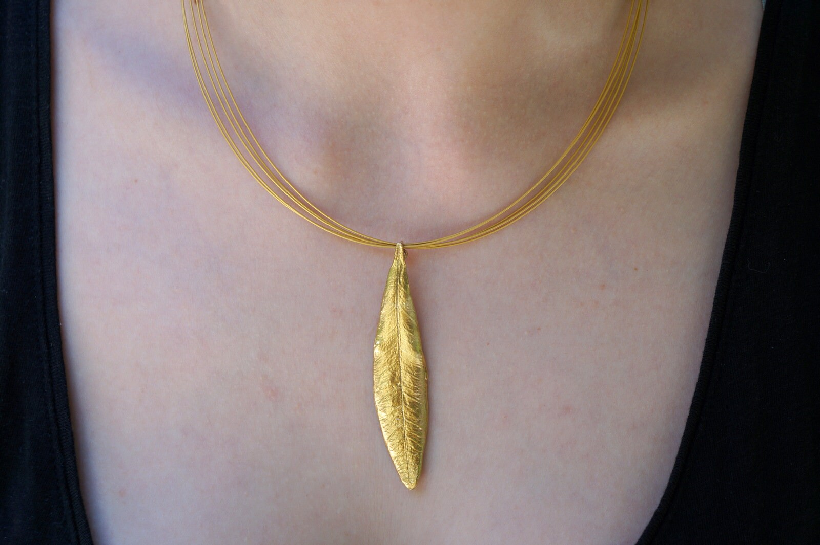 A gold necklace with a large leaf pendant is worn around the neck of a person.