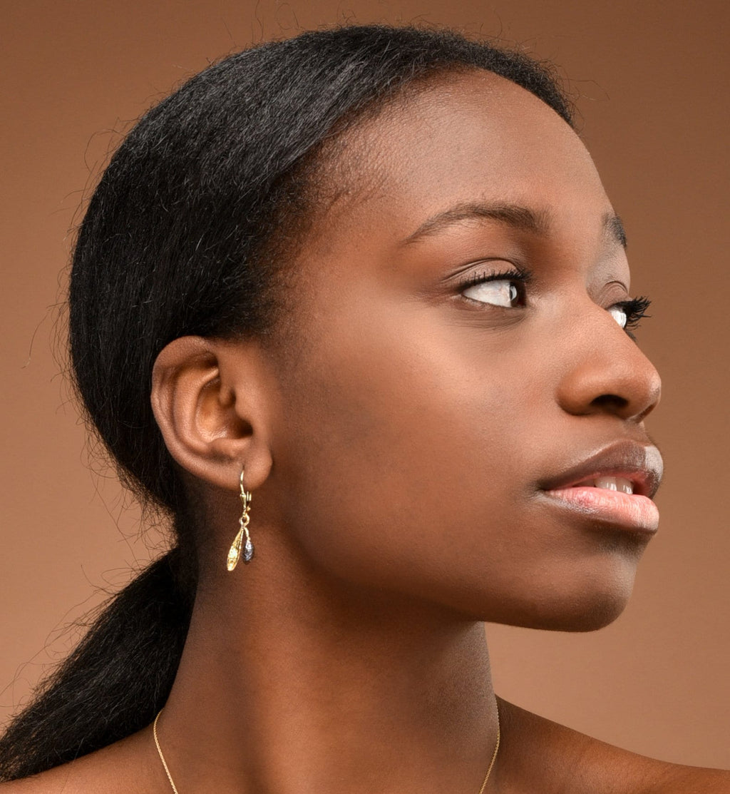 A close-up portrait of a woman with dark hair, wearing a gold earring with dangling stones.