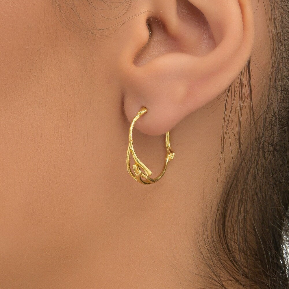 A close-up view of a person's ear wearing a gold-colored hoop earring.