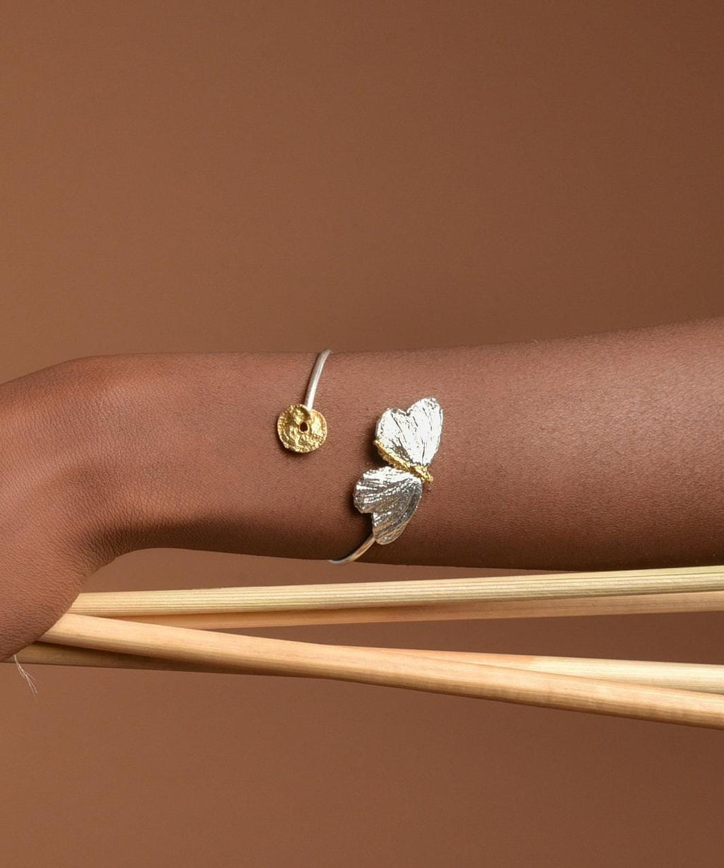 A bracelet with a butterfly design is worn on a person's wrist, set against a brown background.