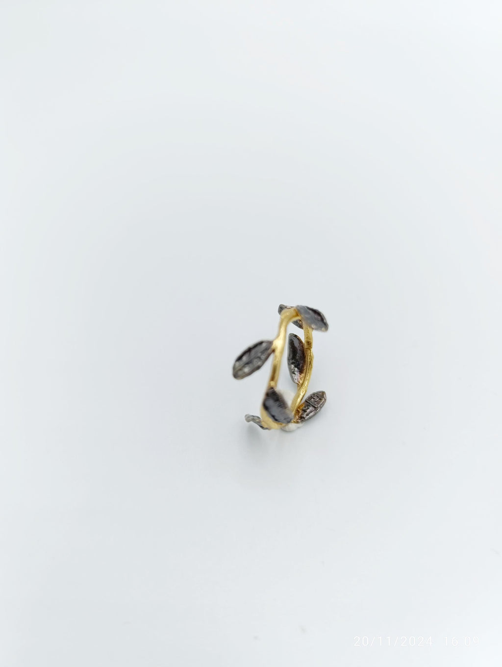 A single ring with a leaf-like design, featuring a combination of gold and black elements, is shown against a plain white background.
