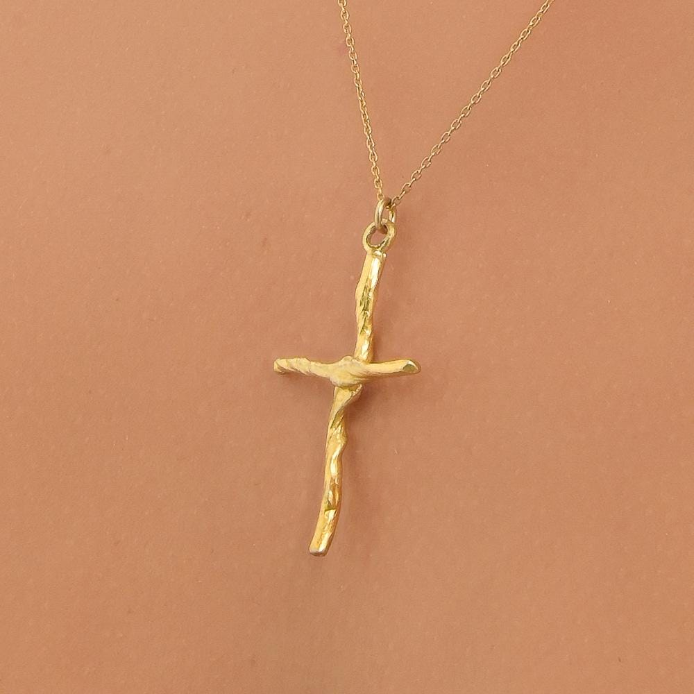 A gold cross pendant necklace is shown against a peach-colored background.
