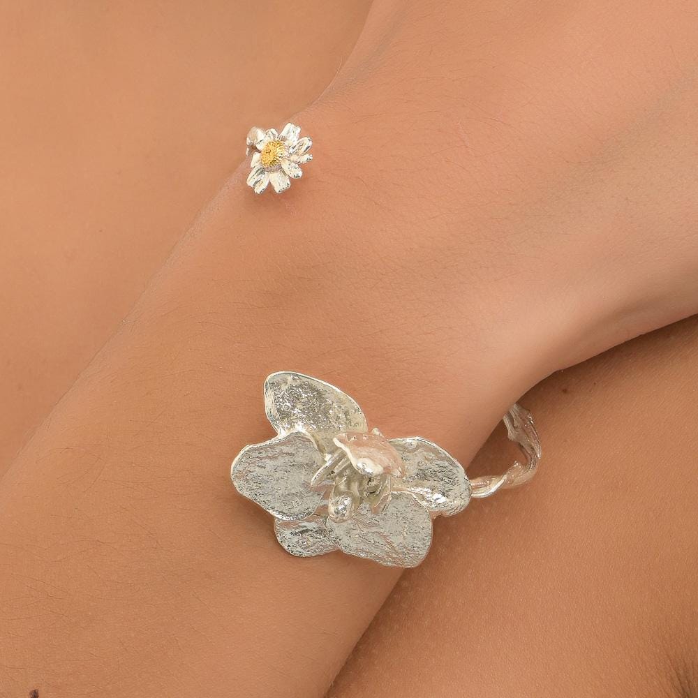 A close-up image of a person's wrist wearing a silver bracelet with a flower-shaped charm.