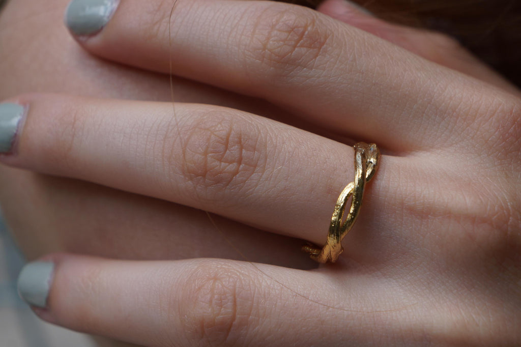 A close-up of a person's hand wearing a gold ring with a twisted design.