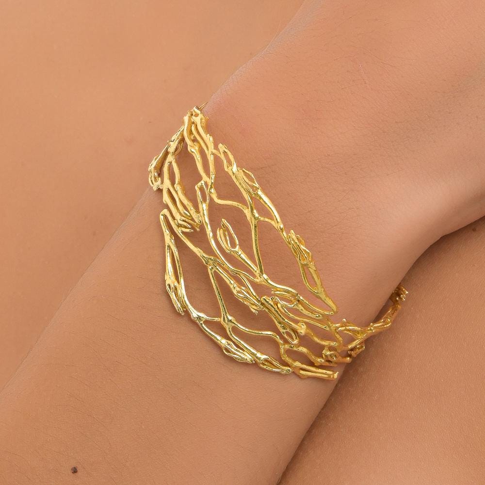 A gold bracelet with intricate, organic-looking designs on a person's wrist.