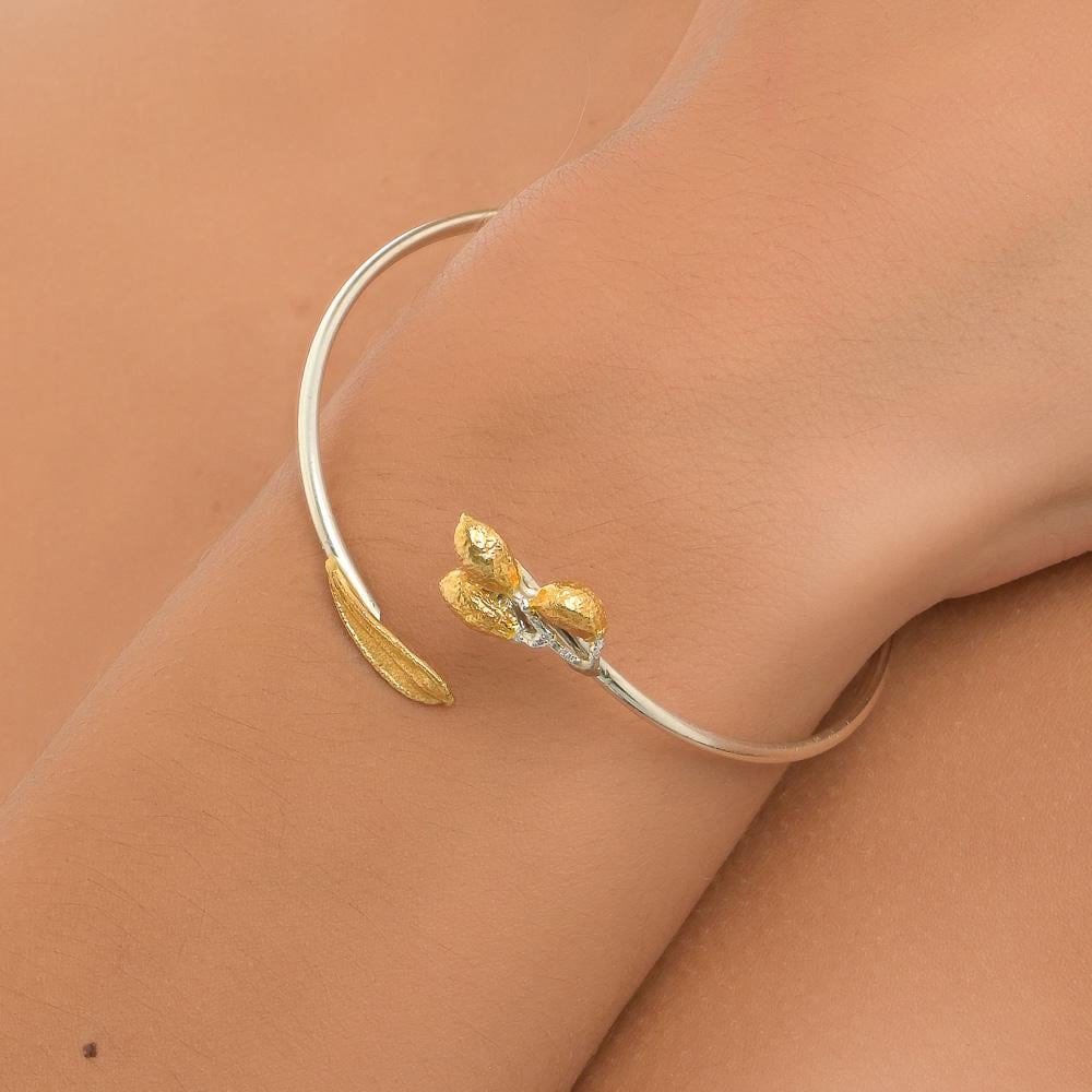 A gold-colored bracelet with a leaf-like design is worn on a person's wrist.