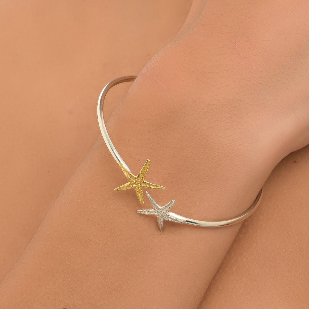 A silver bangle bracelet with two starfish-shaped charms on the wrist.