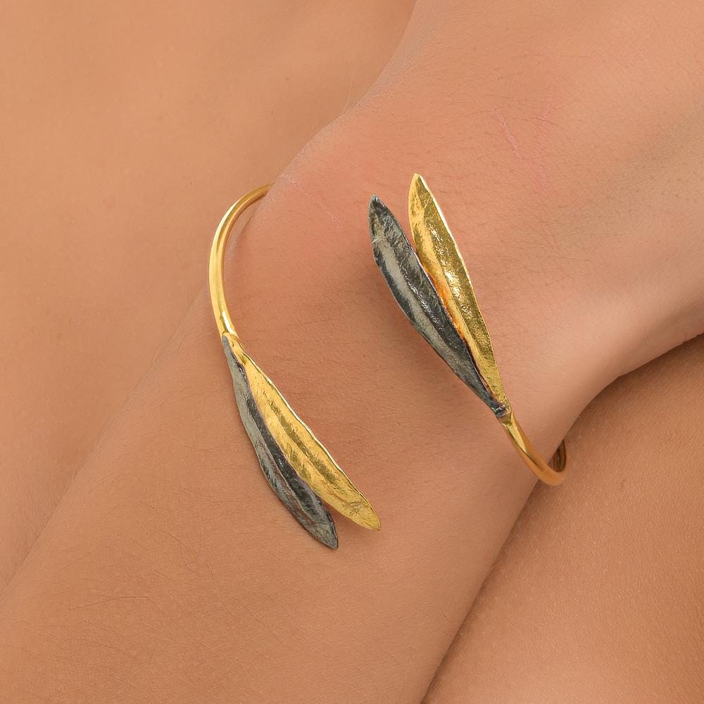 A gold and black leaf-shaped bracelet is worn on a person's wrist.