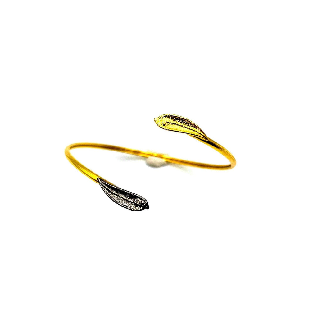 A gold bracelet with two leaf-shaped charms, one gold and one black, is shown against a white background.