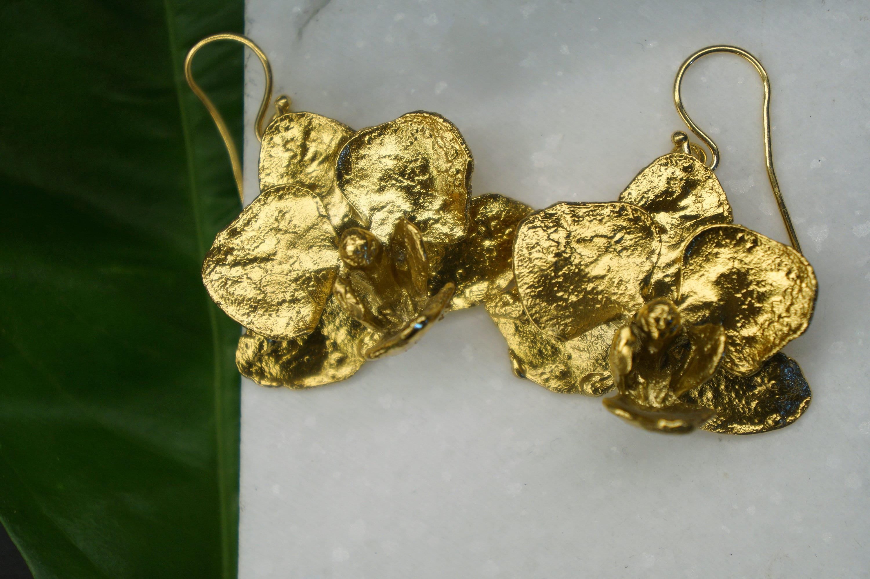 A pair of gold-colored earrings with intricate, textured designs resembling flowers or leaves.