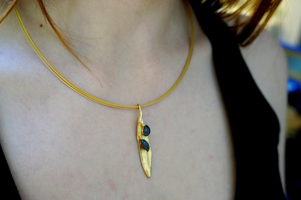 A gold necklace with a pendant featuring two blue stones is worn by a person.