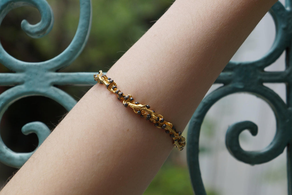 A gold bracelet with black stones is worn on a person's wrist.