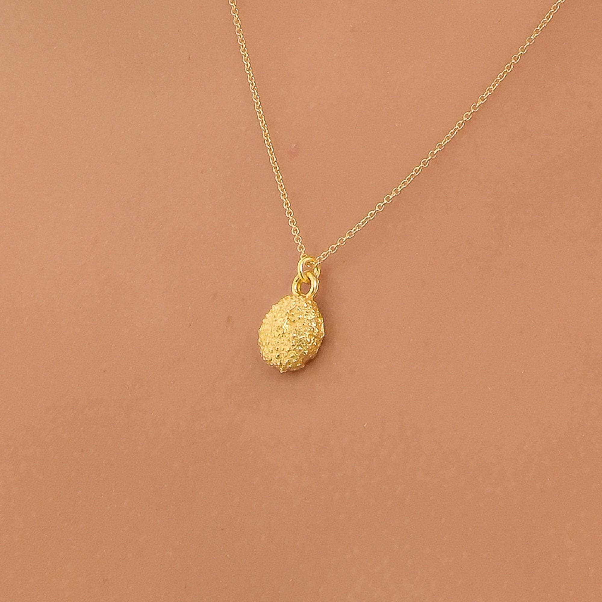 A gold necklace with a round pendant is shown against a peach-colored background.