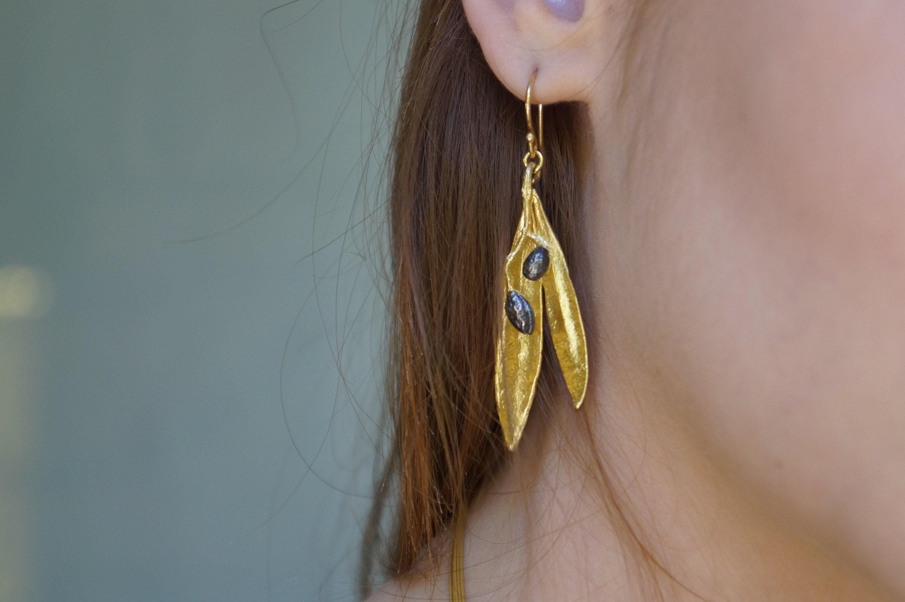 A close-up view of a person's ear wearing a pair of gold earrings with leaf-shaped designs.