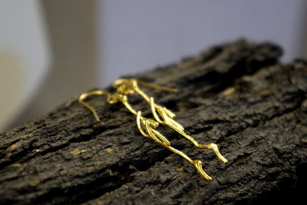 A pair of gold earrings with intricate designs rests on a dark, textured surface.