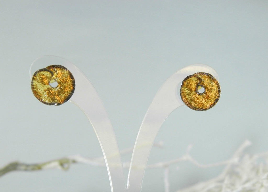 two gold-colored earrings with a metallic texture, displayed on a white stand against a light blue background.