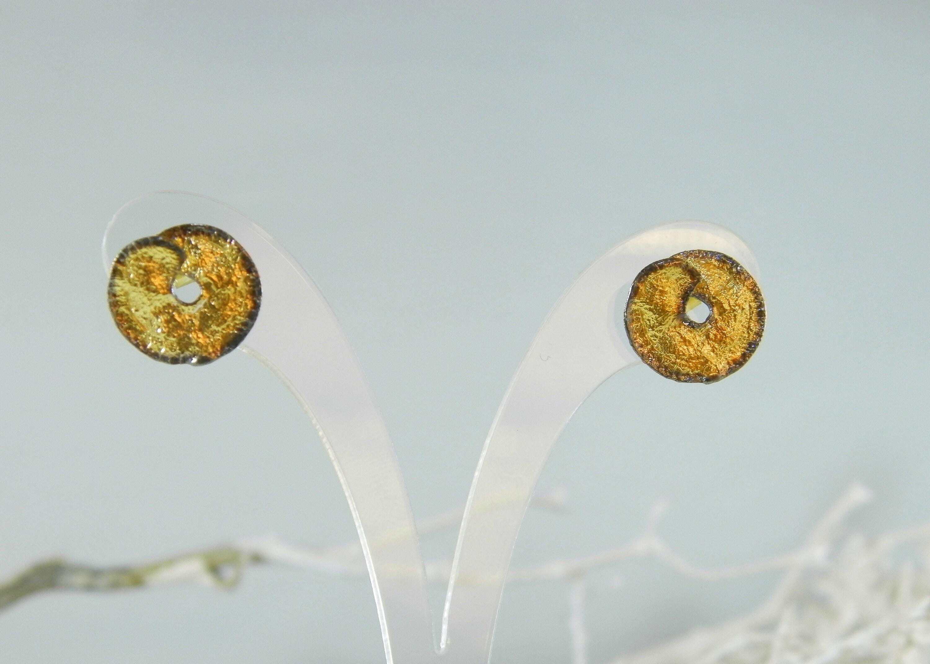 two gold-colored earrings with a metallic texture, displayed on a white stand against a light blue background.