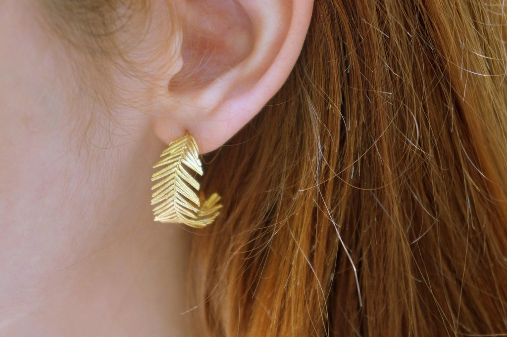 A close-up view of a person's ear wearing a gold earring shaped like a leaf.
