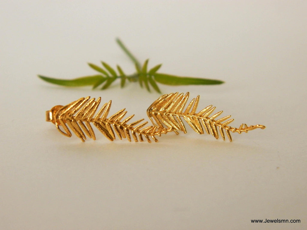 a pair of gold leaf earrings with intricate leaf designs, placed on a white surface.