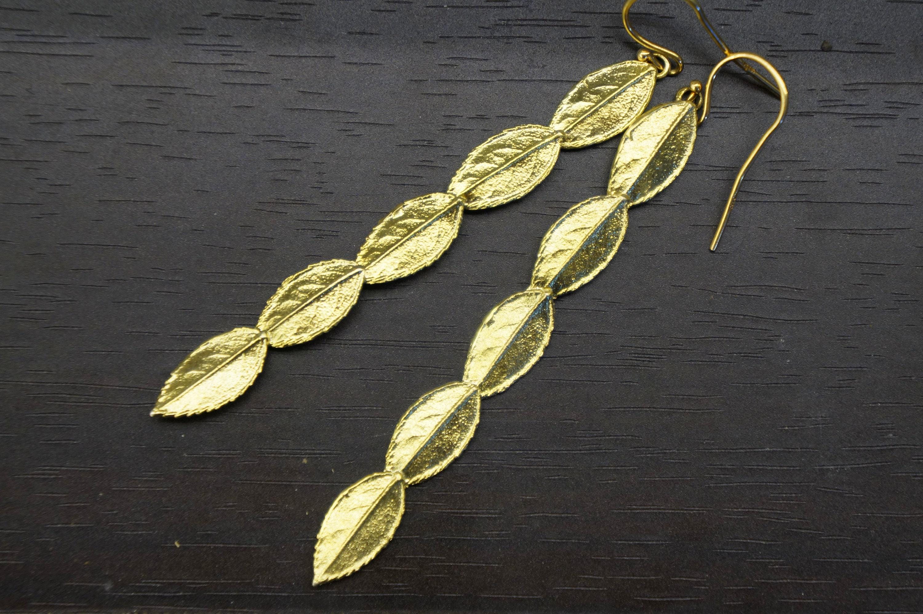 A pair of gold leaf earrings with a leaf design, resting on a dark surface.