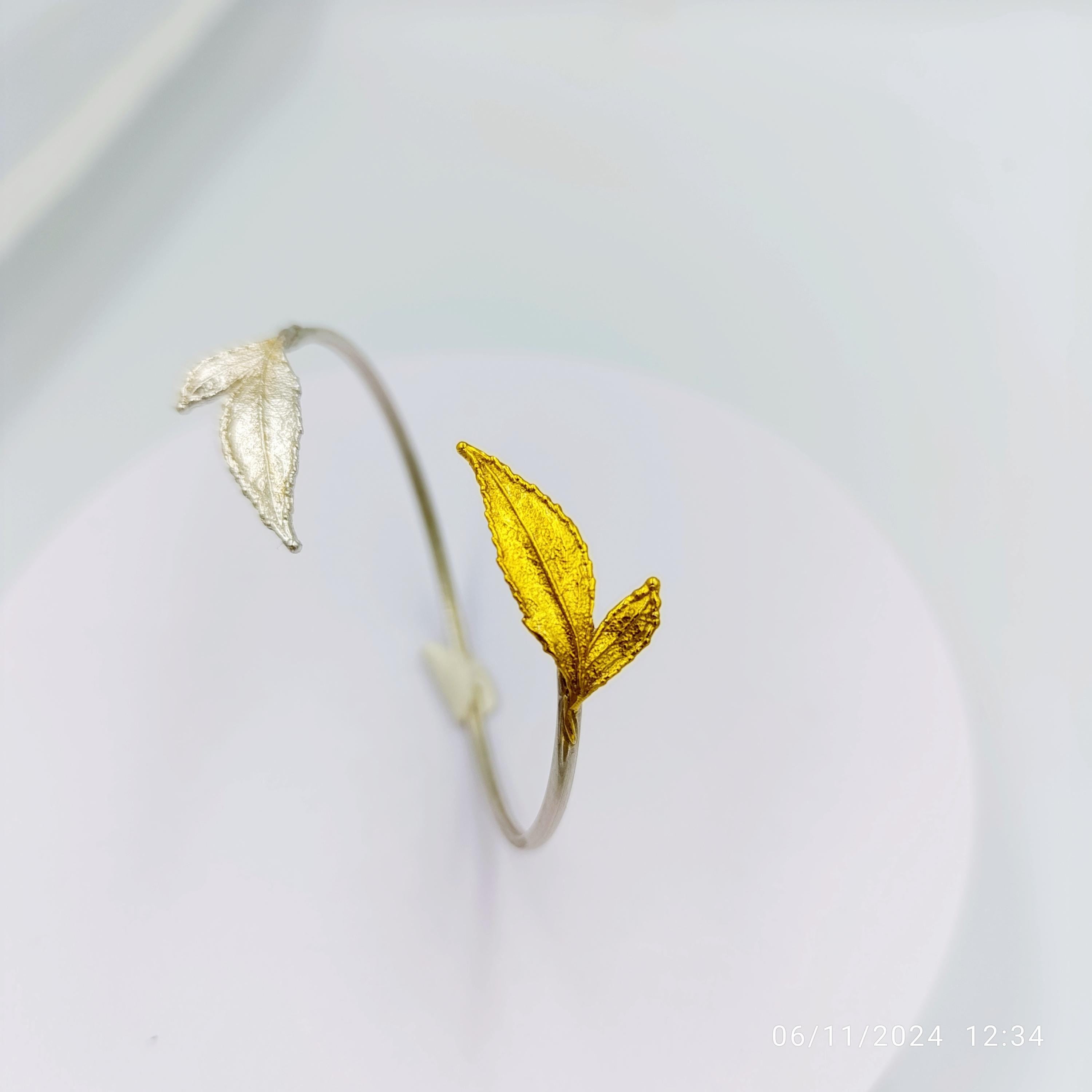 A close-up image of a silver bracelet with a yellow leaf-shaped charm on it, set against a white background.