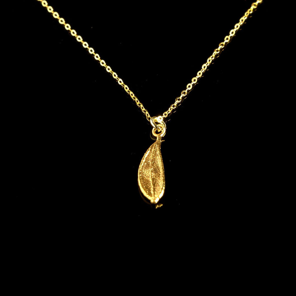 A gold-colored necklace with a single pendant, which appears to be a leaf-shaped charm, is displayed against a black background.