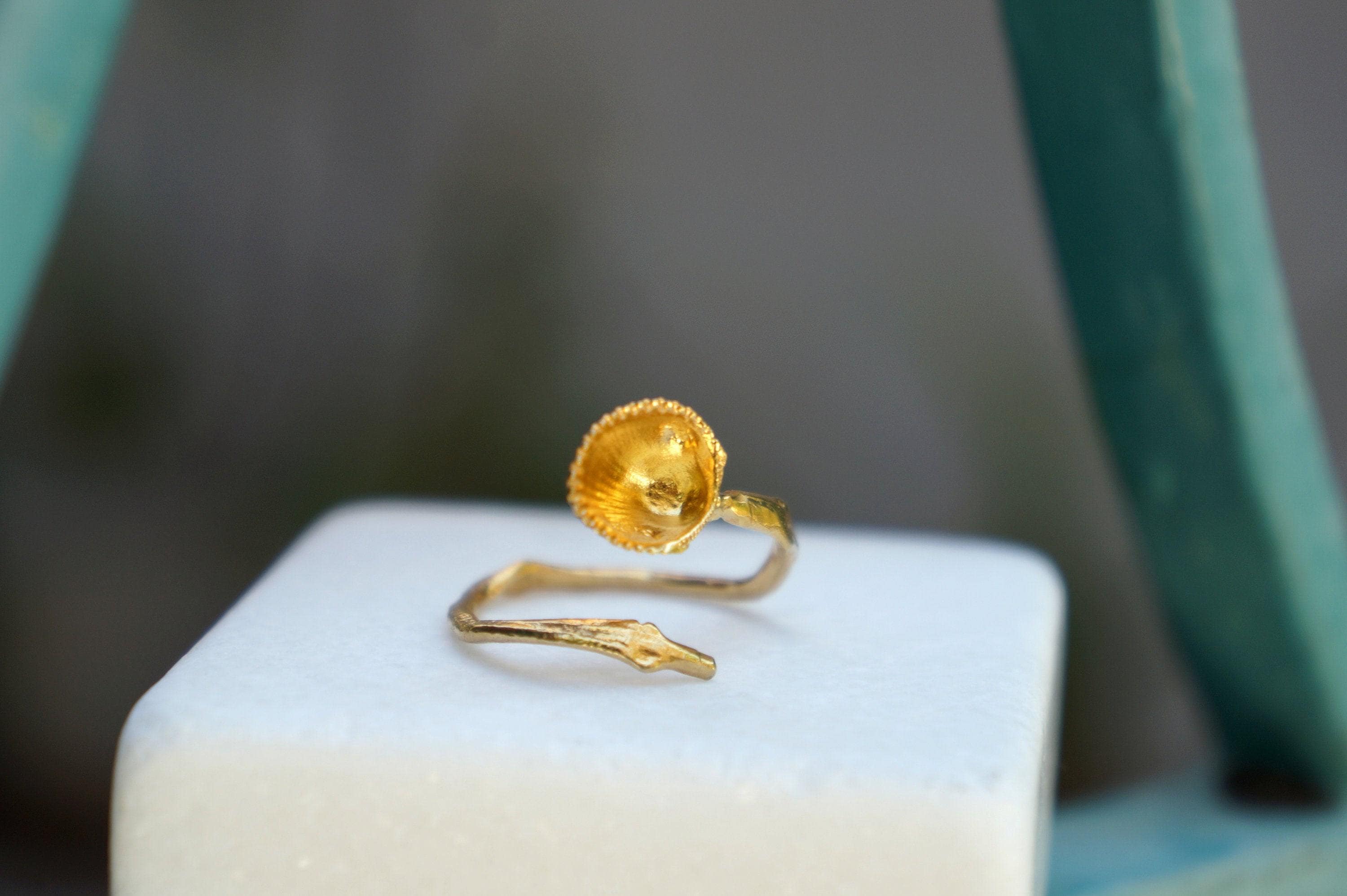 A gold ring with a flower-like design sits on a white surface, with a blurred green background.