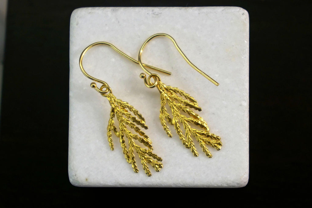 A pair of gold earrings with leaf-shaped designs, displayed on a white surface against a black background.