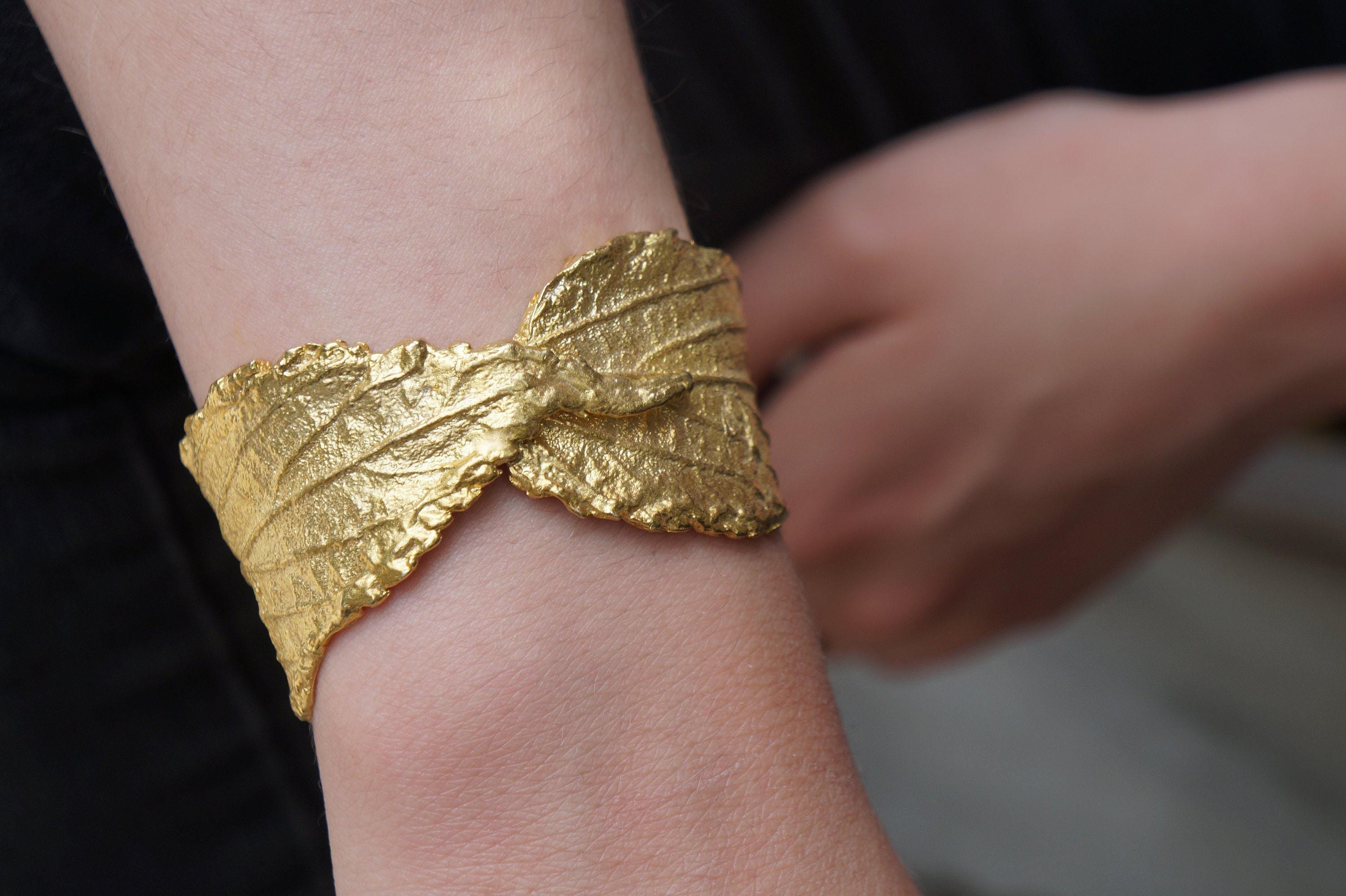 A gold leaf bracelet is worn on a person's wrist.