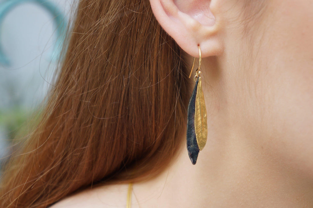 A close-up view of a person's ear wearing a pair of gold and black earrings.