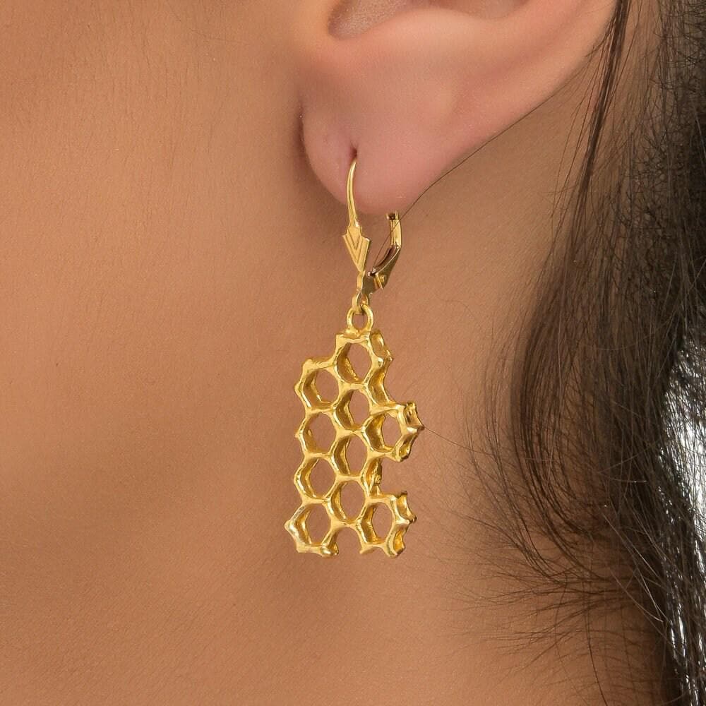 A close-up view of a gold earring with a honeycomb design hanging from the ear.