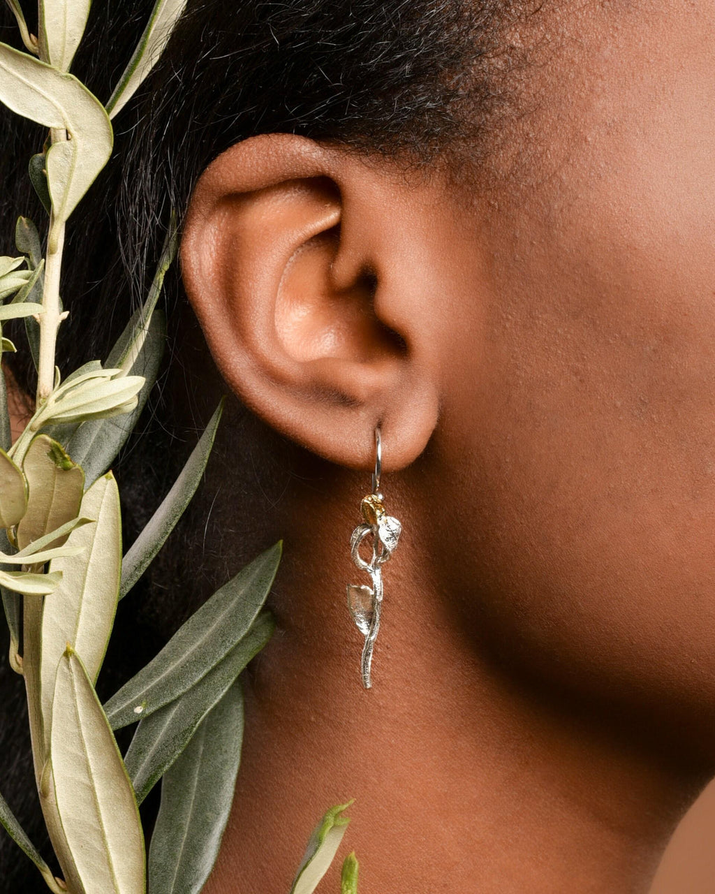 A close-up view of a person's ear adorned with a pair of silver earrings featuring a floral design.