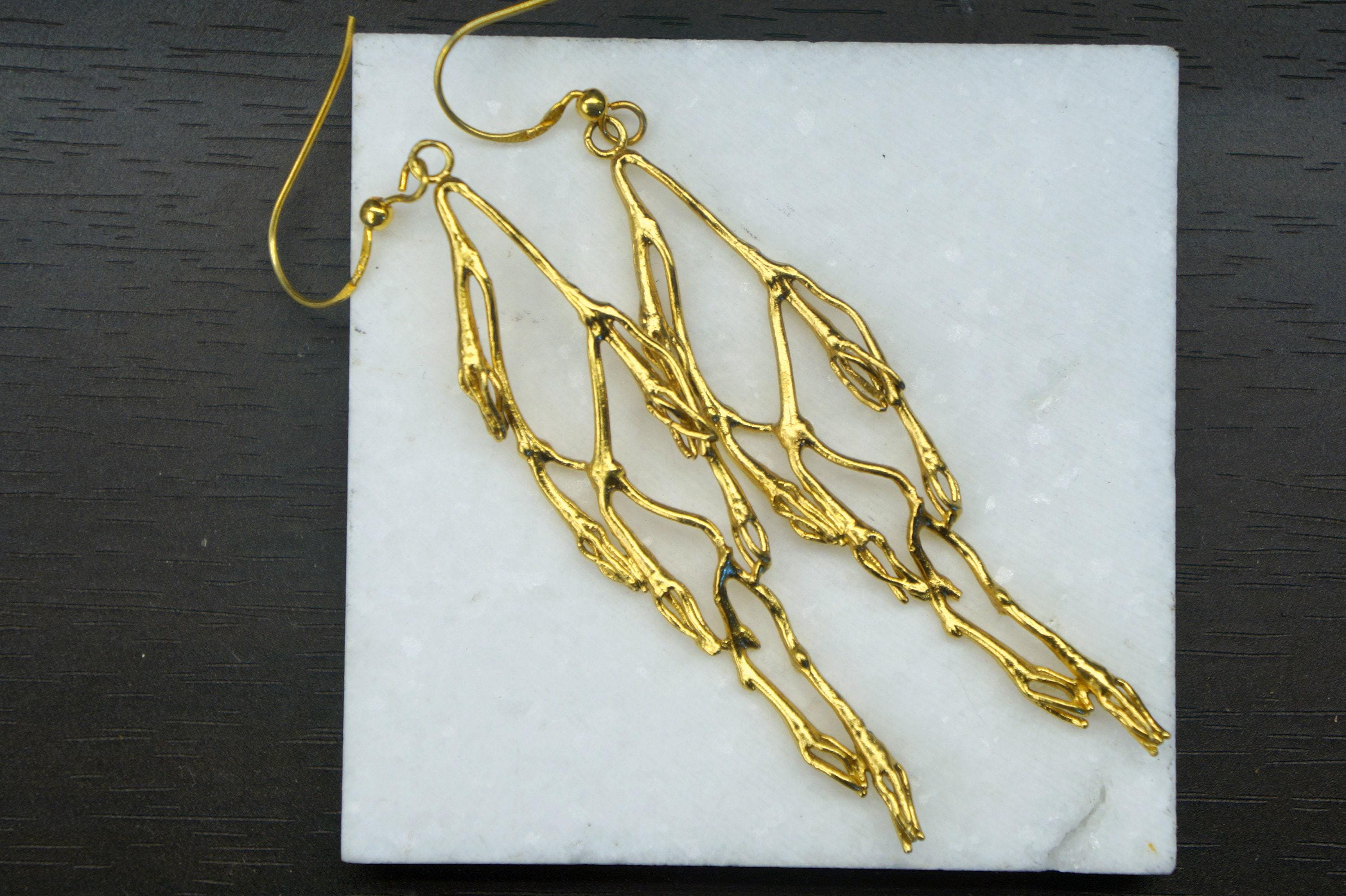 A pair of gold earrings with intricate, organic designs resting on a white marble surface.
