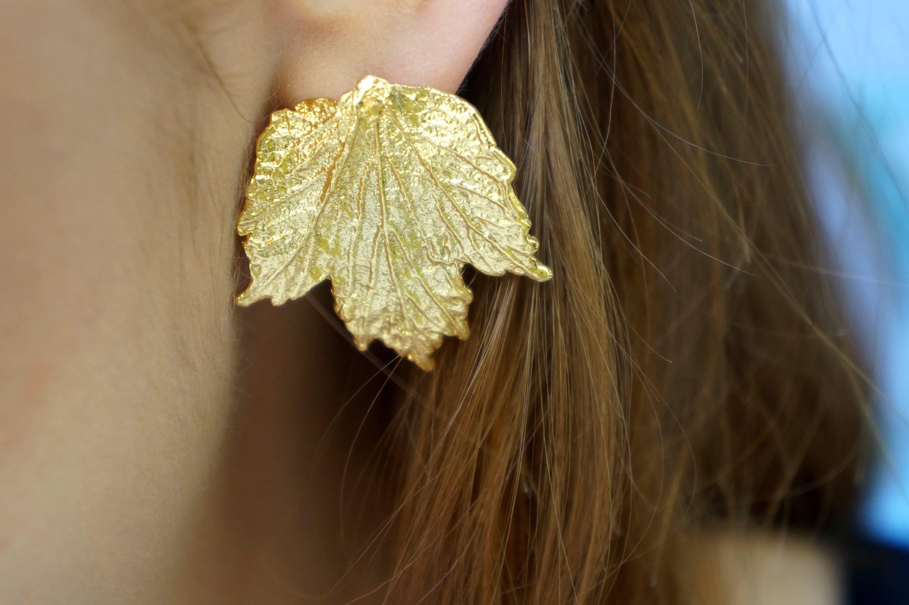 A close-up of a person's ear wearing a gold leaf earring.