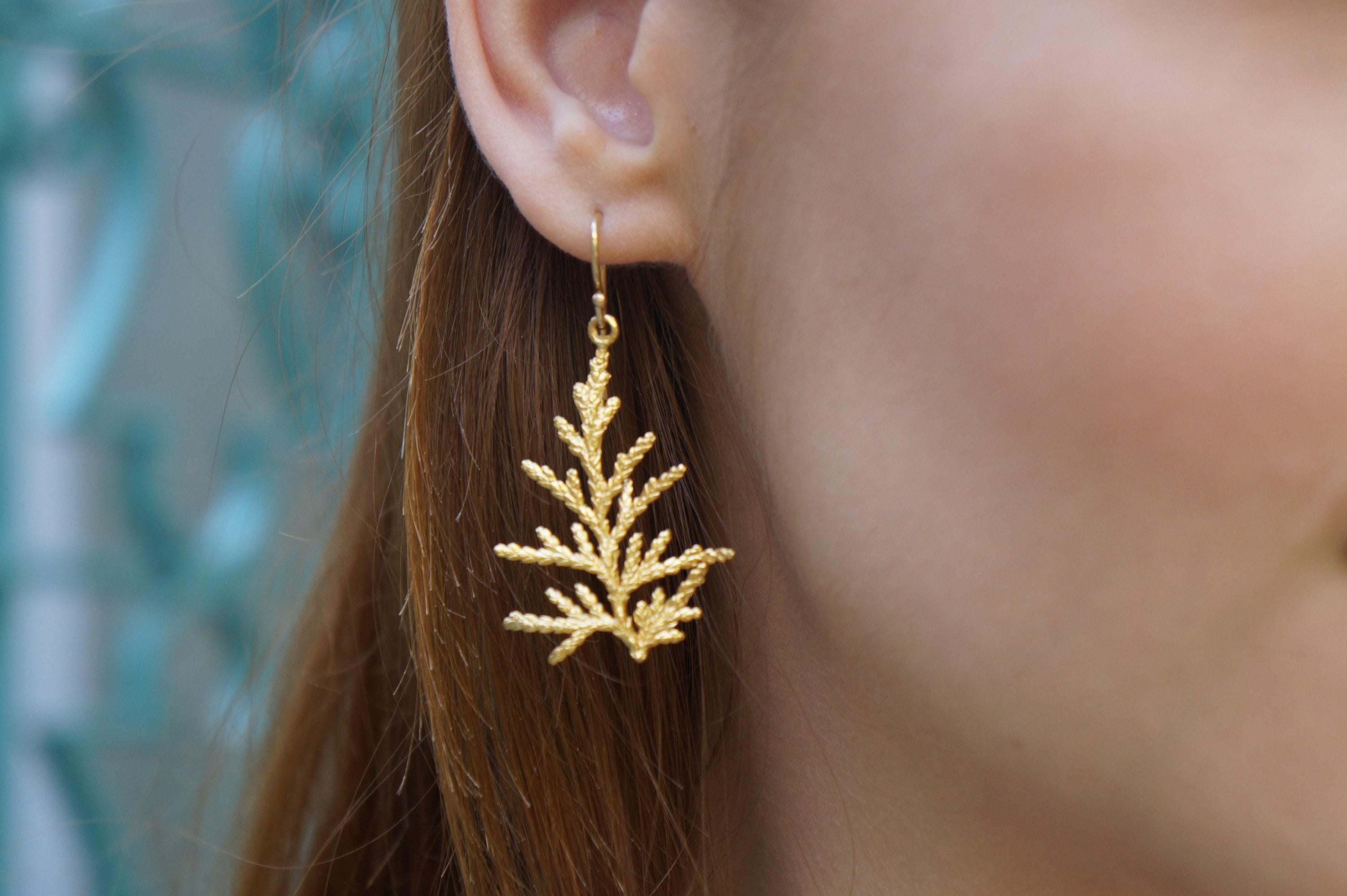 A close-up view of a person's ear wearing a gold earring shaped like a leaf or branch.