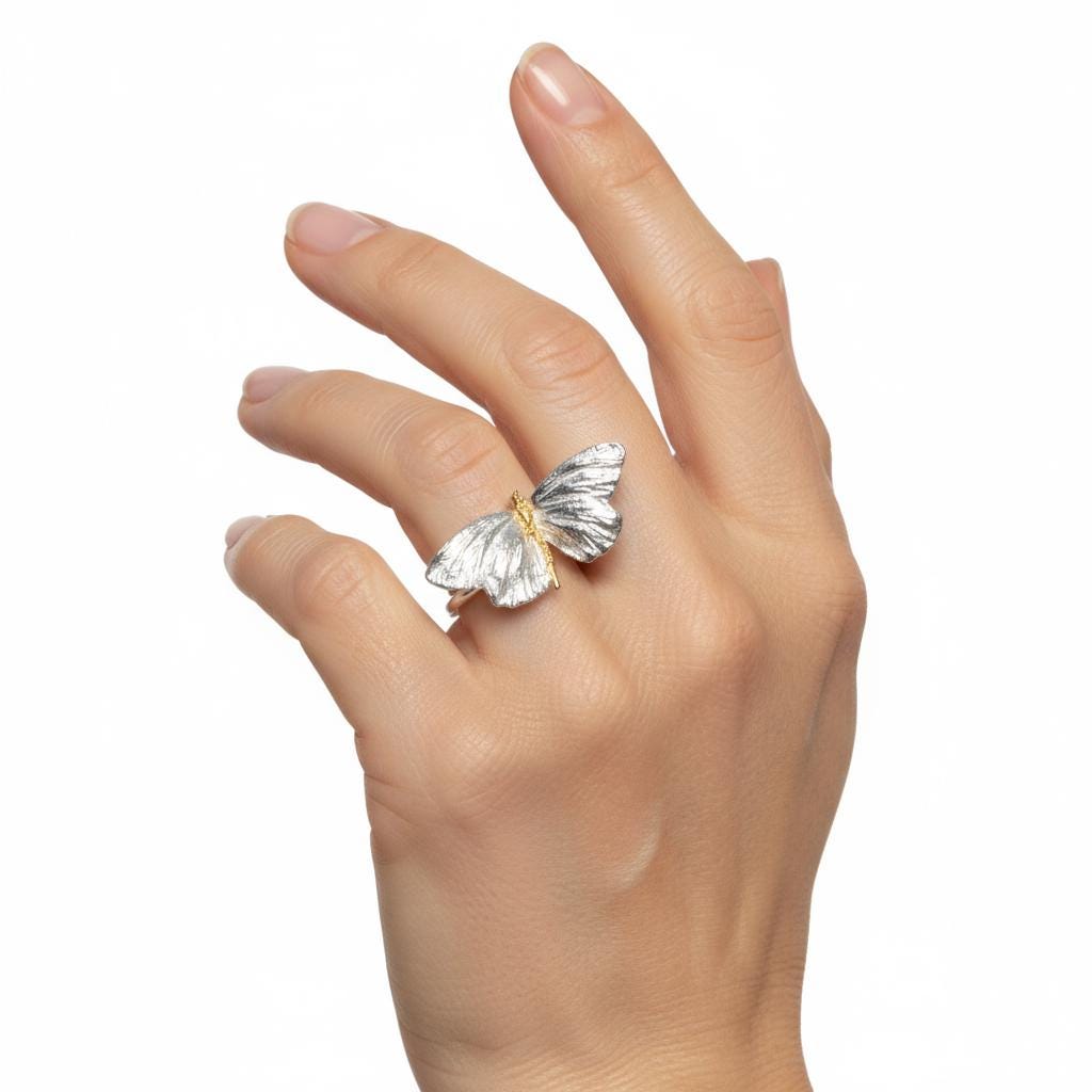 A hand wearing a silver and gold butterfly ring is shown in the image.