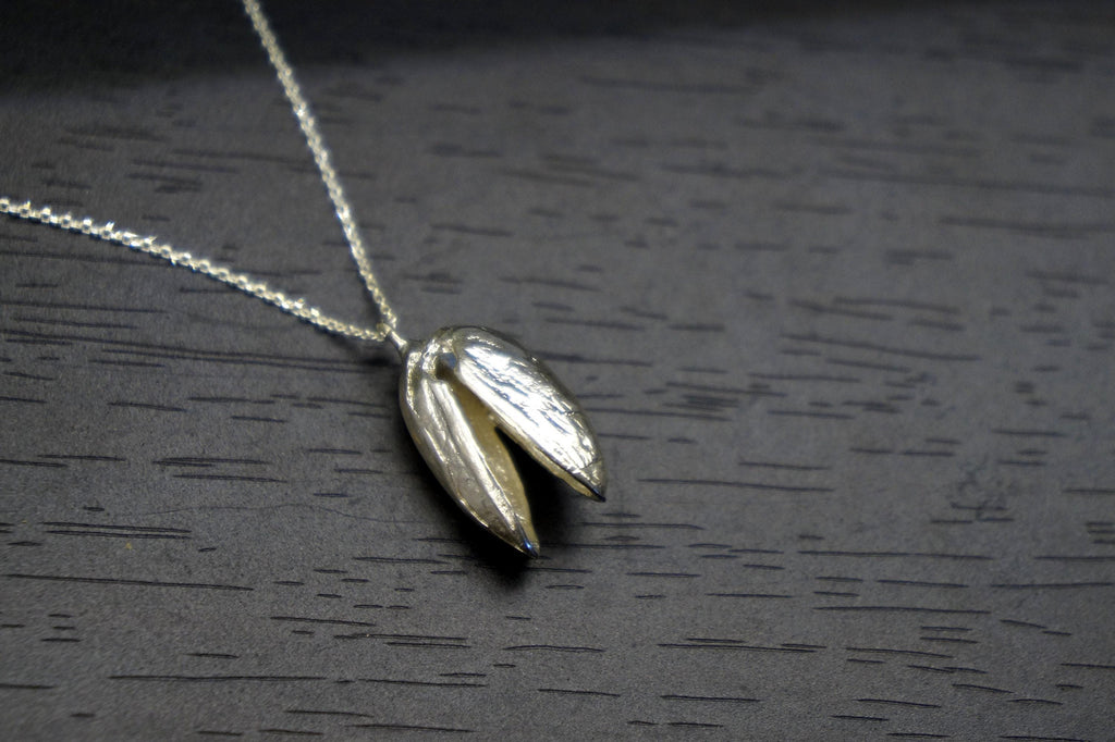 A silver necklace with a pendant is displayed on a dark surface.