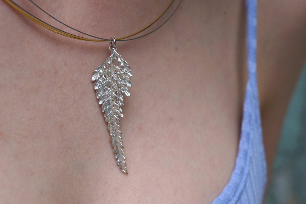 A close-up view of a silver feather pendant hanging from a necklace.