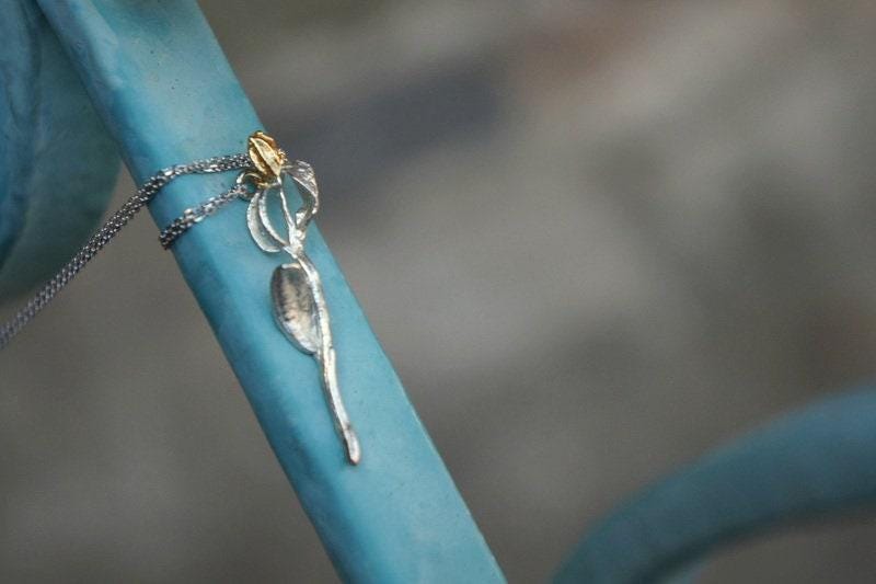 A close-up view of a silver pendant with a gold-colored charm hanging from a chain, attached to a blue metal surface.