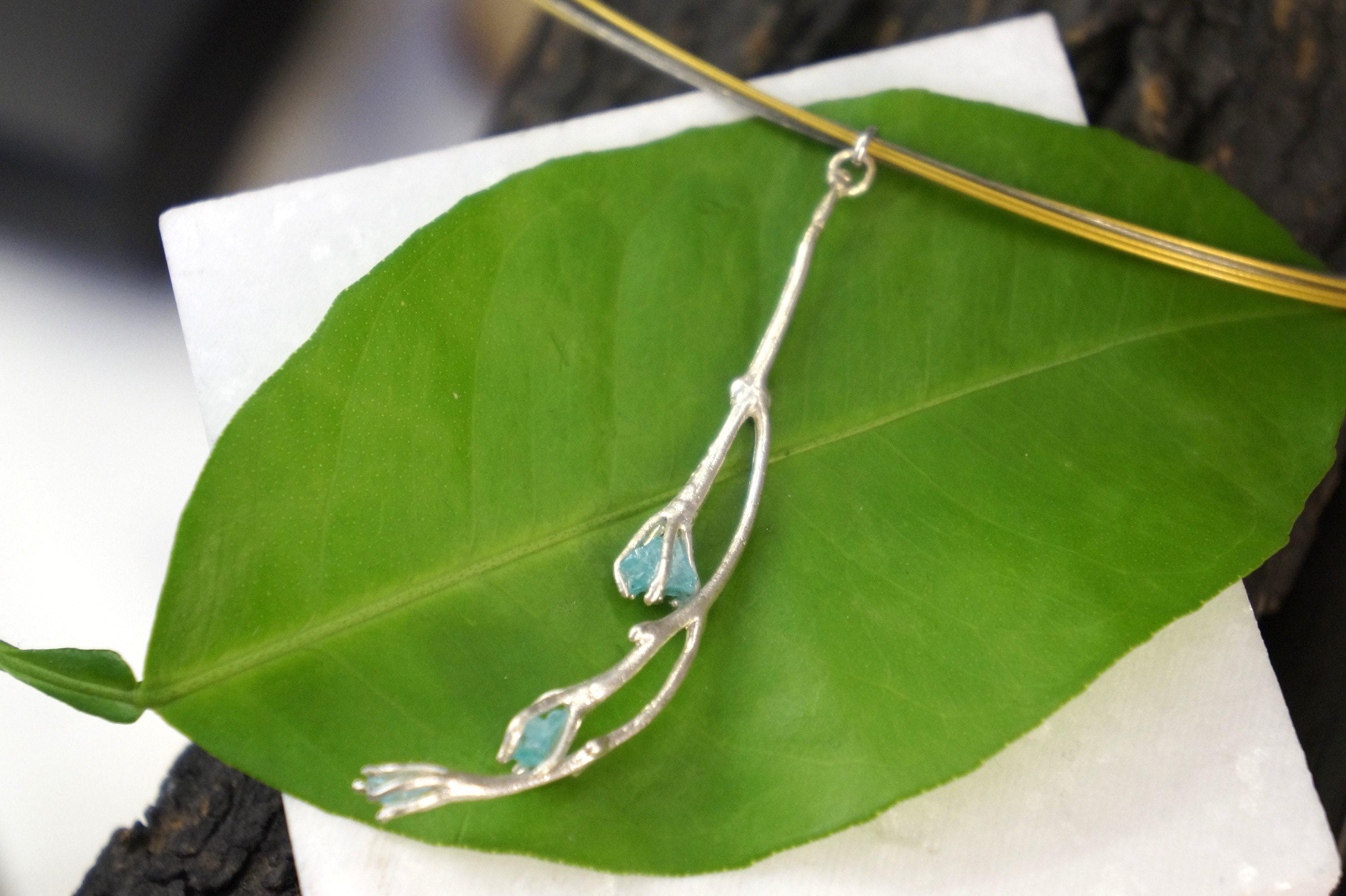 A silver leaf-shaped pendant with blue stones is displayed on a white surface.