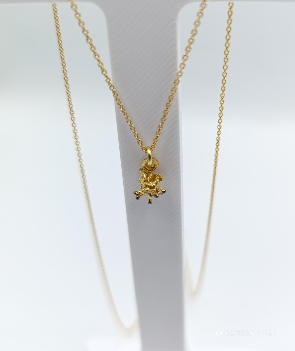 A delicate gold-colored necklace with a small pendant in the center, hanging from a white stand.