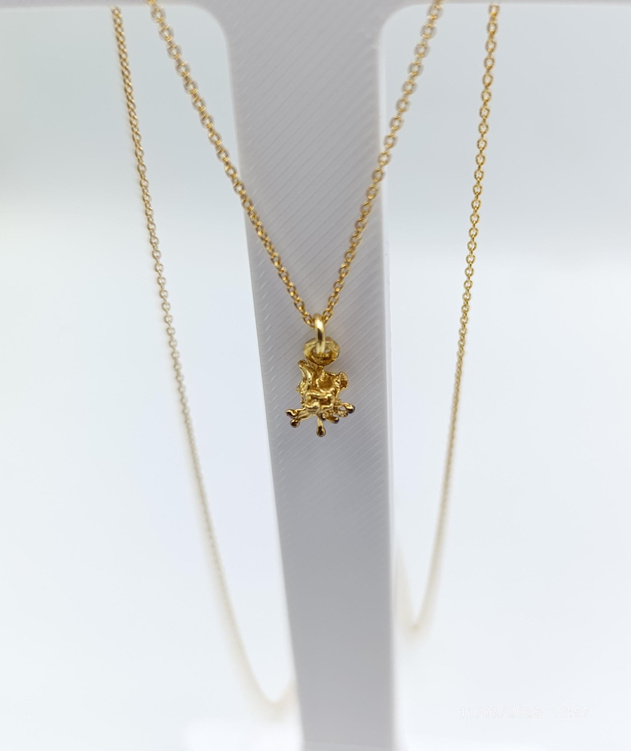 A delicate gold-colored necklace with a small pendant in the center, hanging from a white stand.
