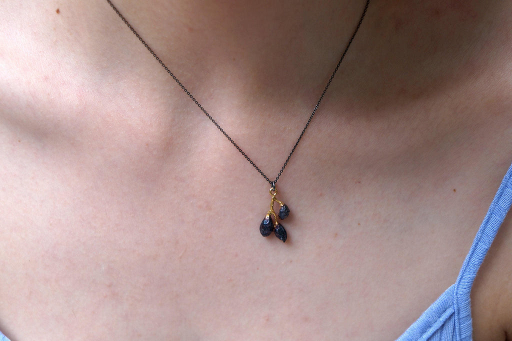 A close-up view of a person's neck and chest area, showing a delicate necklace with a pendant featuring three blue stones.