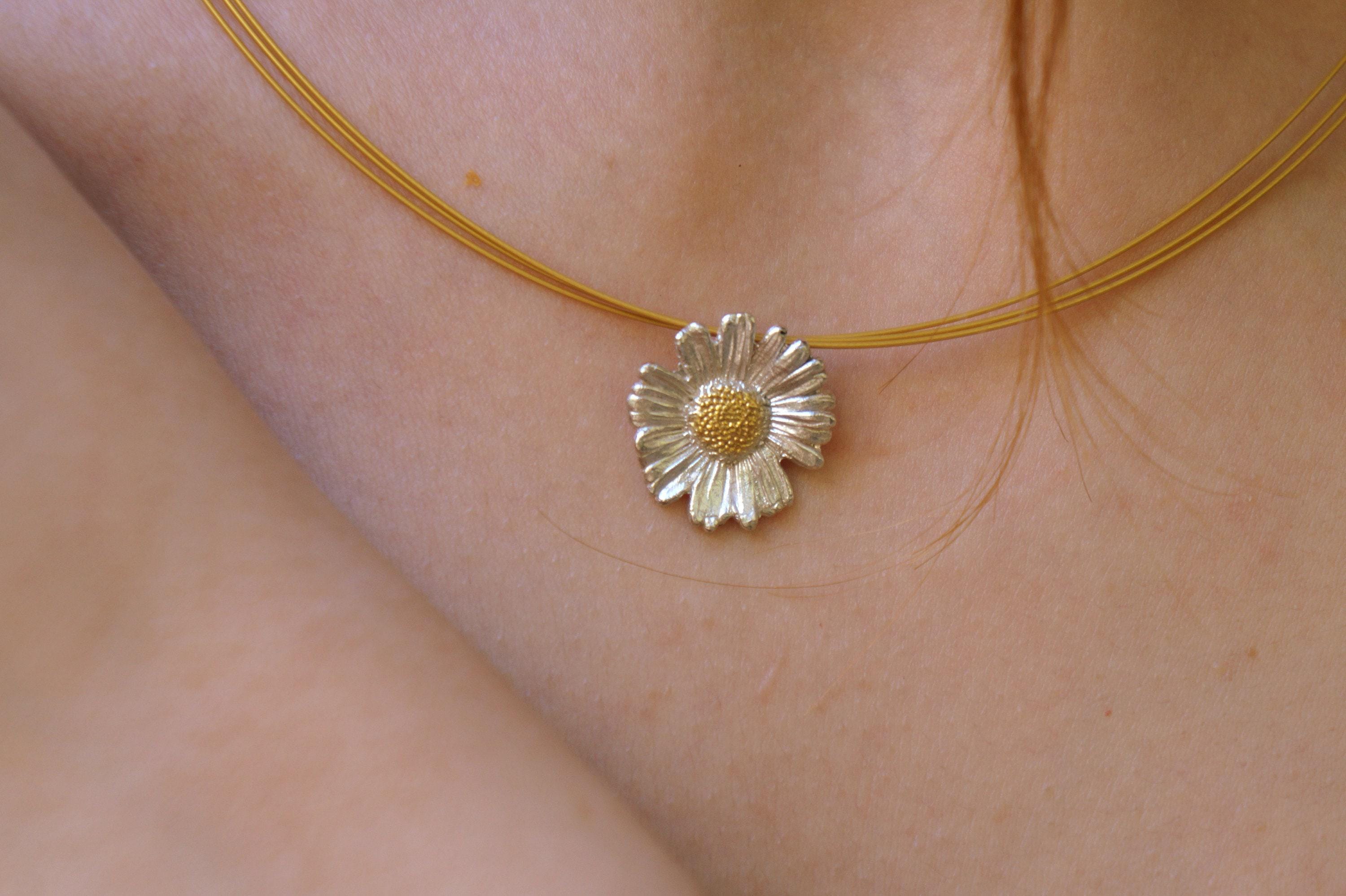 A close-up view of a person's neck and chest area, with a delicate gold-toned necklace featuring a small, intricately designed flower pendant.
