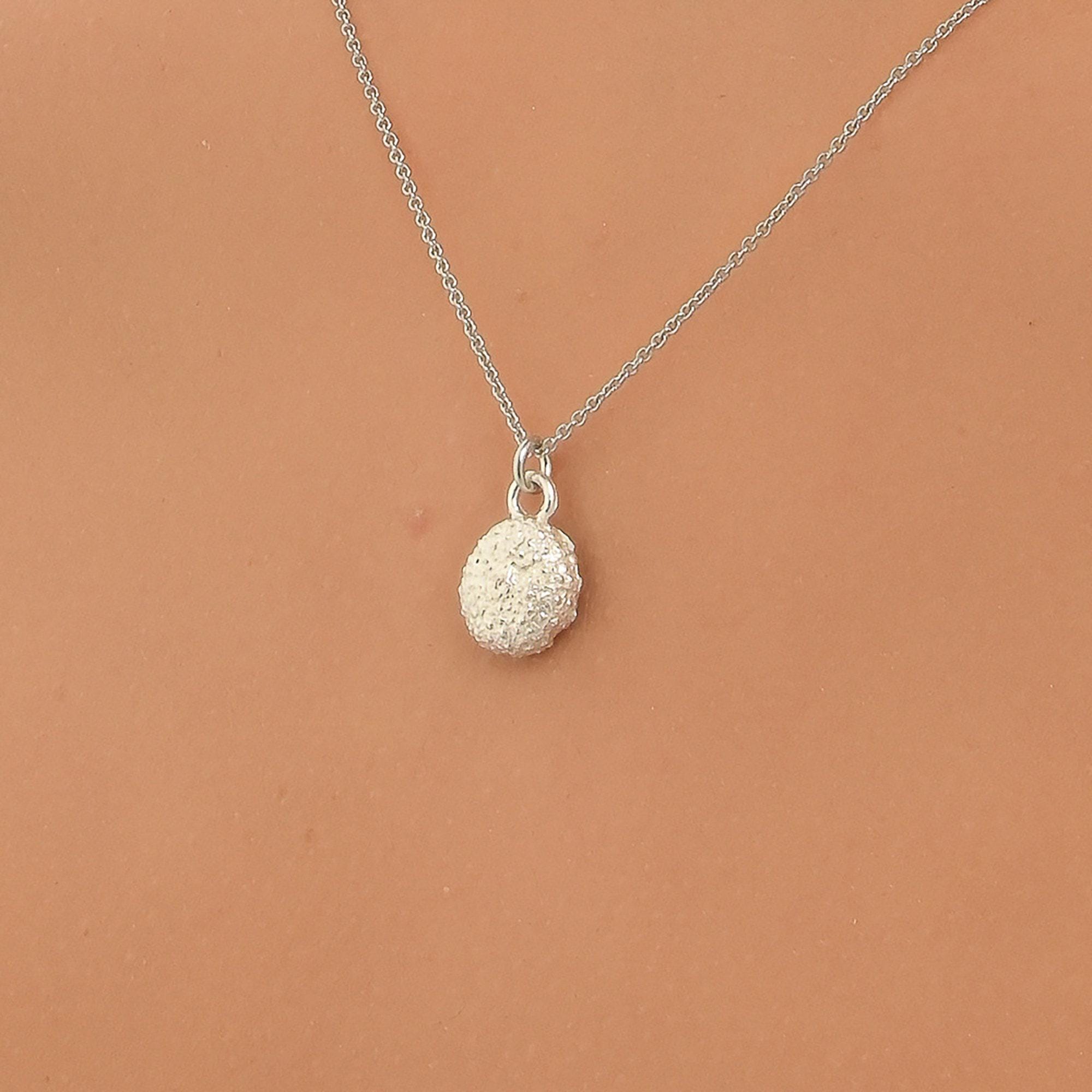 A silver necklace with a round pendant is shown against a peach-colored background.